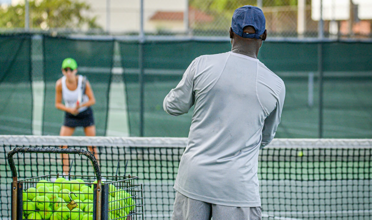 College tennis coach and a player during practice.